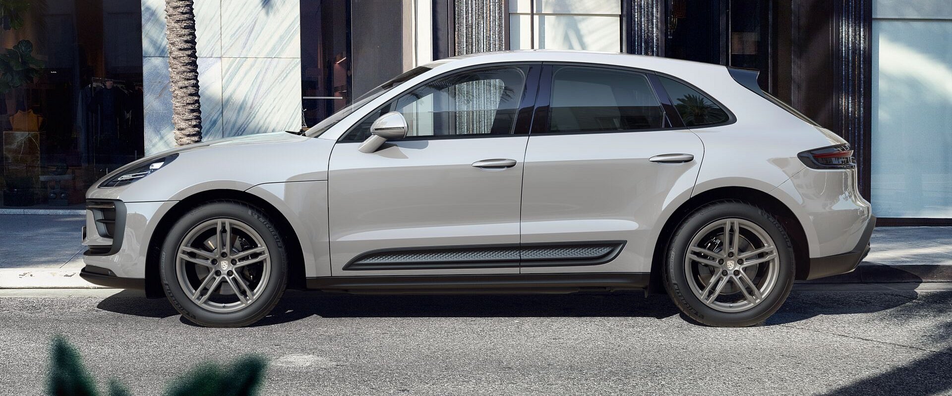 A side angle of a Chalk colored porsche macan sitting in a luxury shopping strip